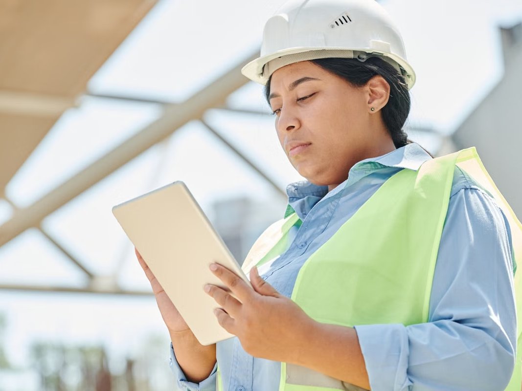 Safety inspector in a hard hat and high-visibility vest reviewing a checklist on a tablet